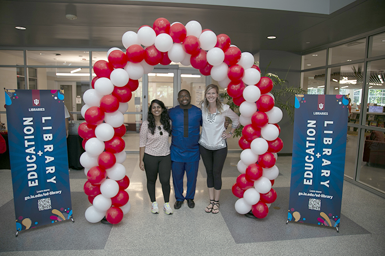 Three people stand together in a pose underneath a red and white balloon arch