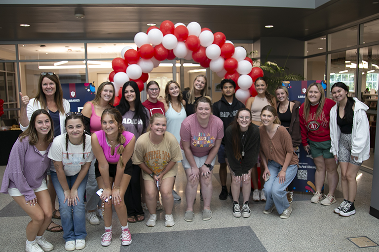 A large group of students stands in front of a red and white balloon arch