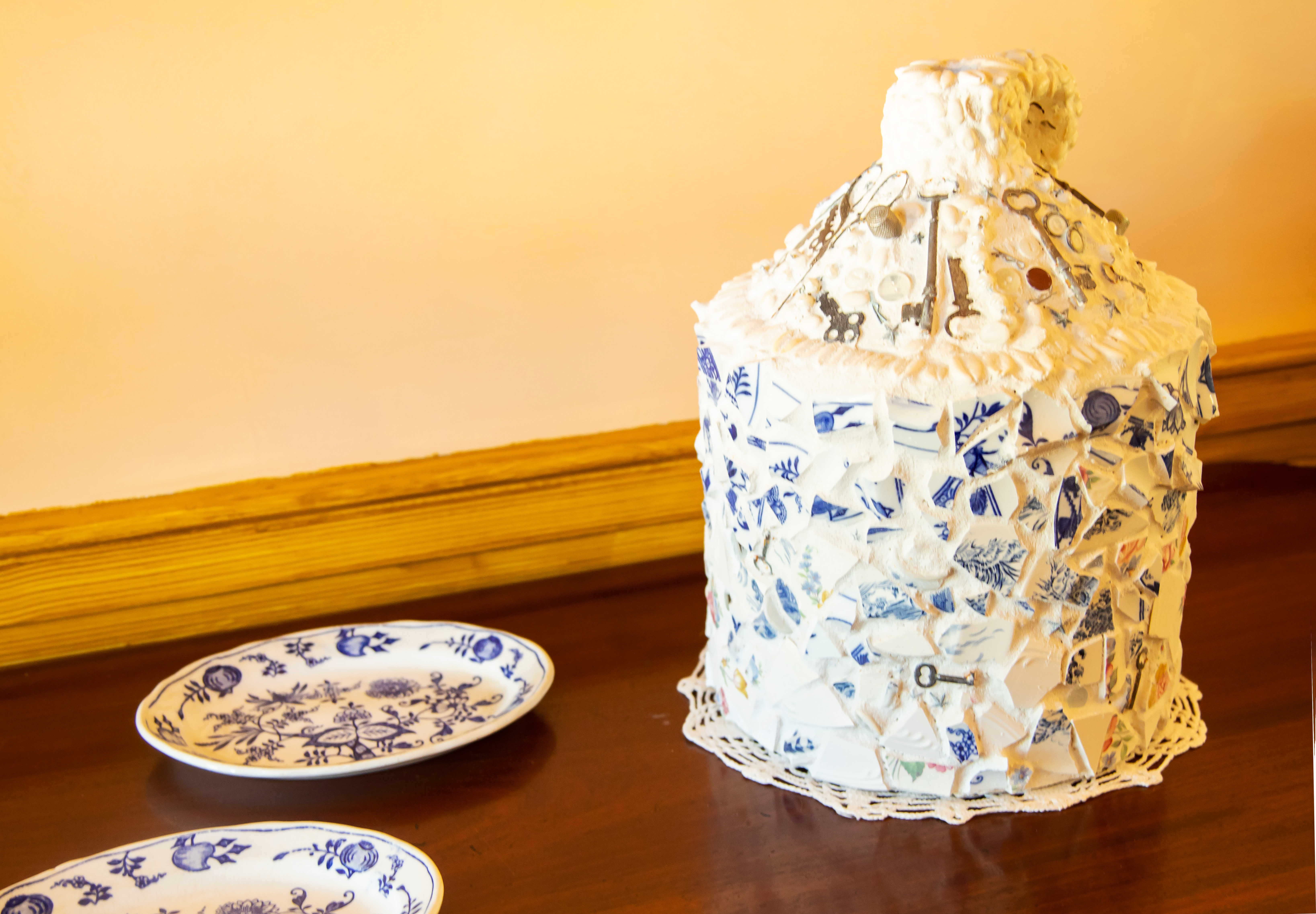 Memory jug art. A jug covered in white plaster with blue tiles and small trinkets embedded.