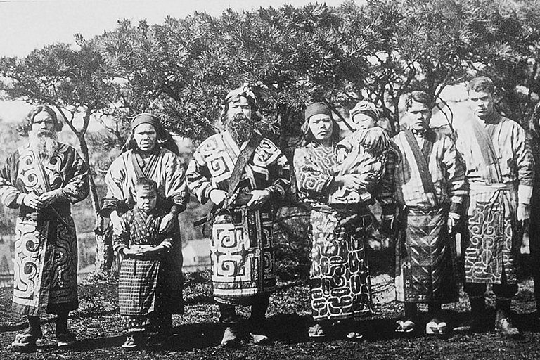 A group of Ainu people stand in native clothes facing the camera.