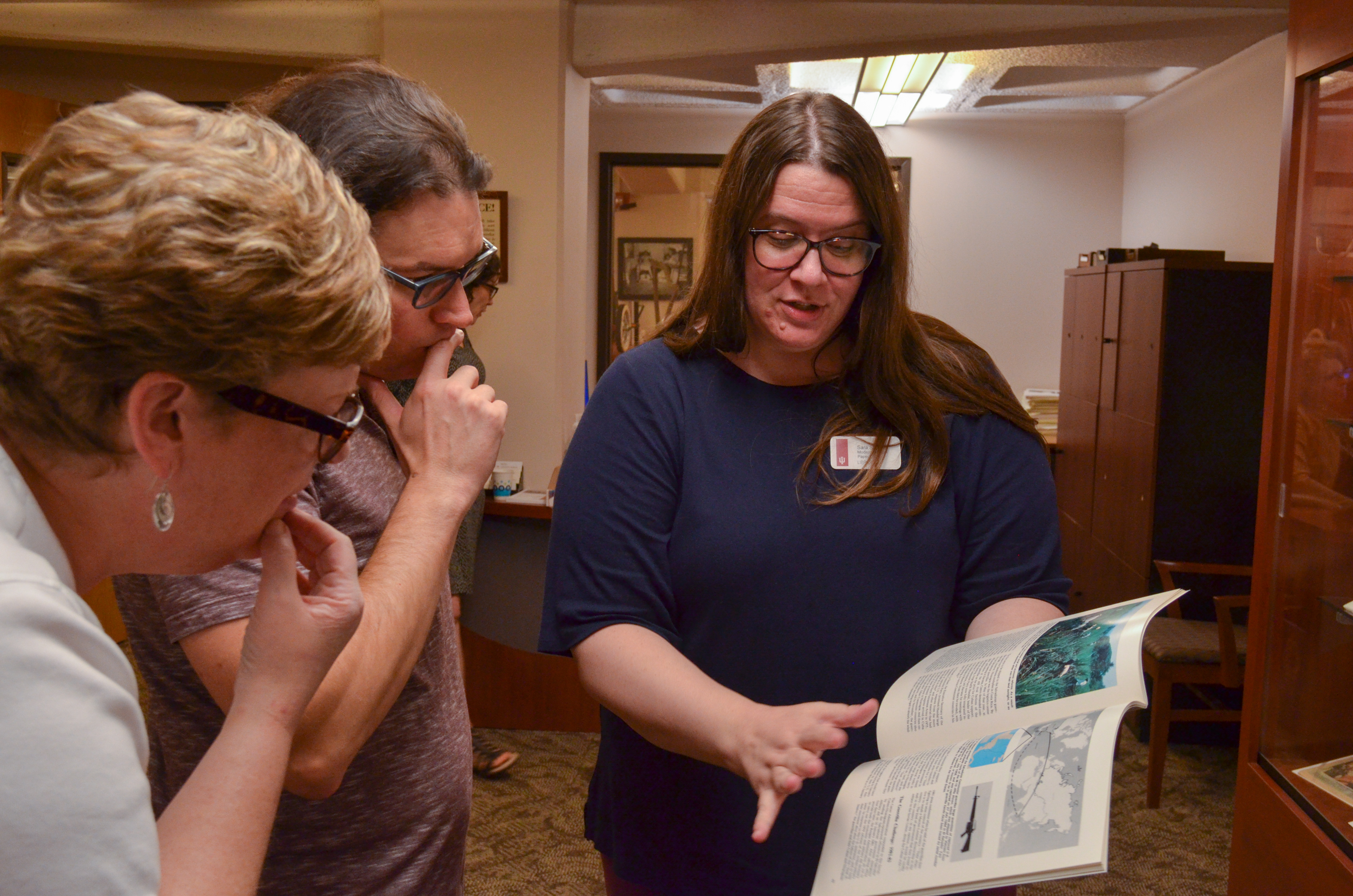 A woman showing a book to two individuals.