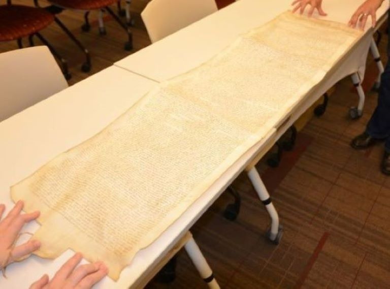 A long scroll unrolled on a table. It's covered in cursive handwriting.