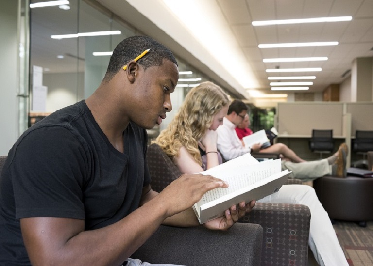 Male Student reading a book in Derner Reading Corner in East Tower of Wells Library 2015