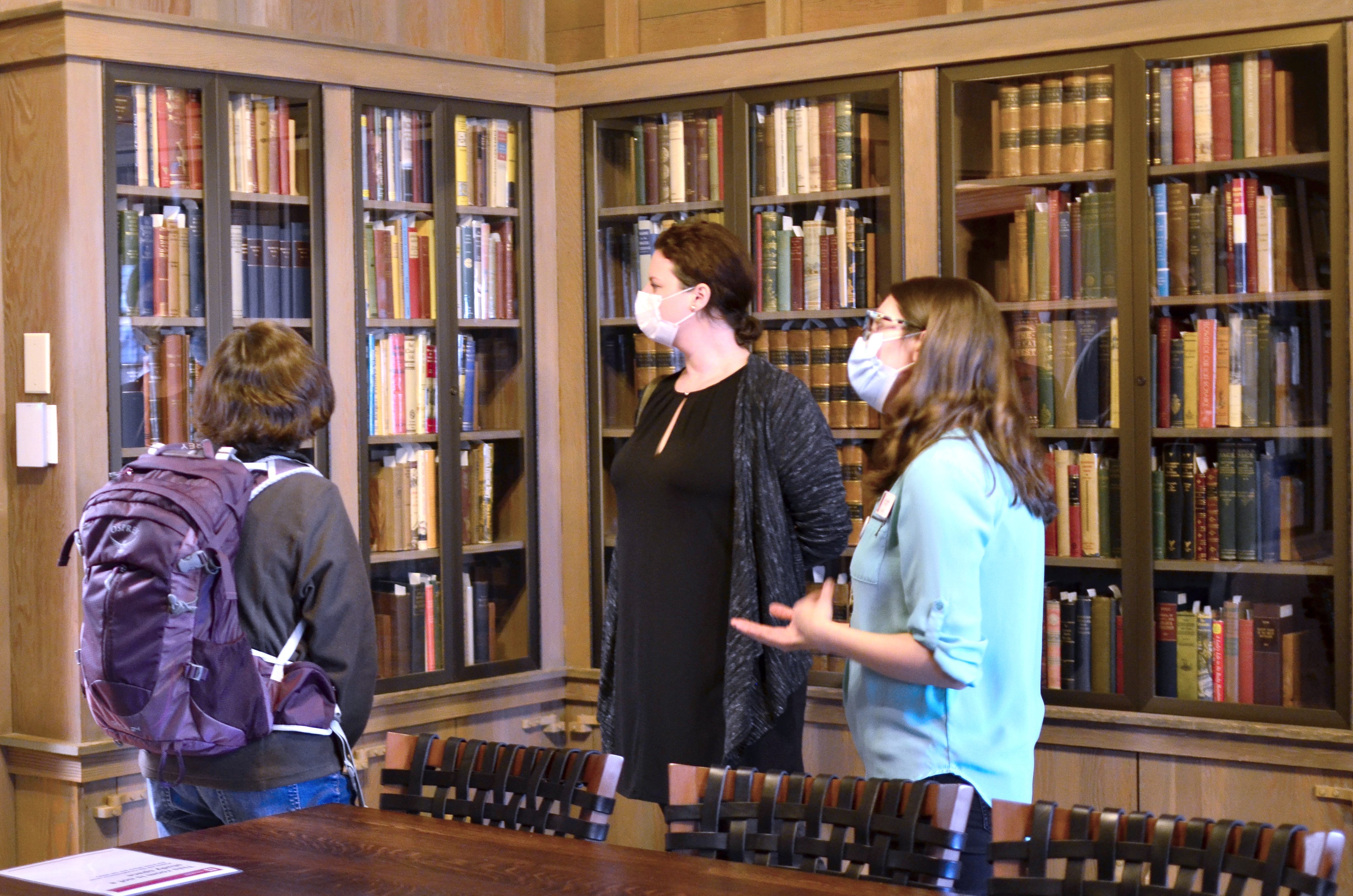 As part of a tour of the Lilly Library, a librarian talks about some of the books on display in the Ellison Room while two tour participants listen.