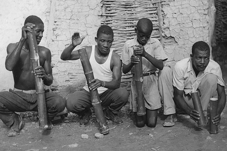 Haitian musicians squat on the ground and play bamboo stampers.