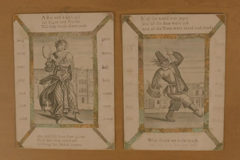 Two cards featuring 18th century images of children at play rest side by side on a wooden table.