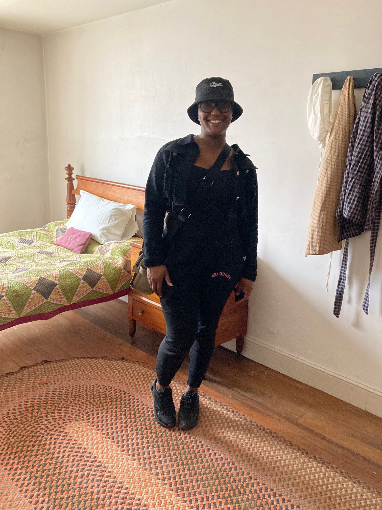 Young black woman standing in attic bedroom in front of antique bed