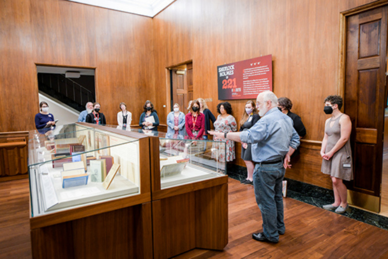 A man points towards a display case in the Lilly Library as members of a tour group look on.