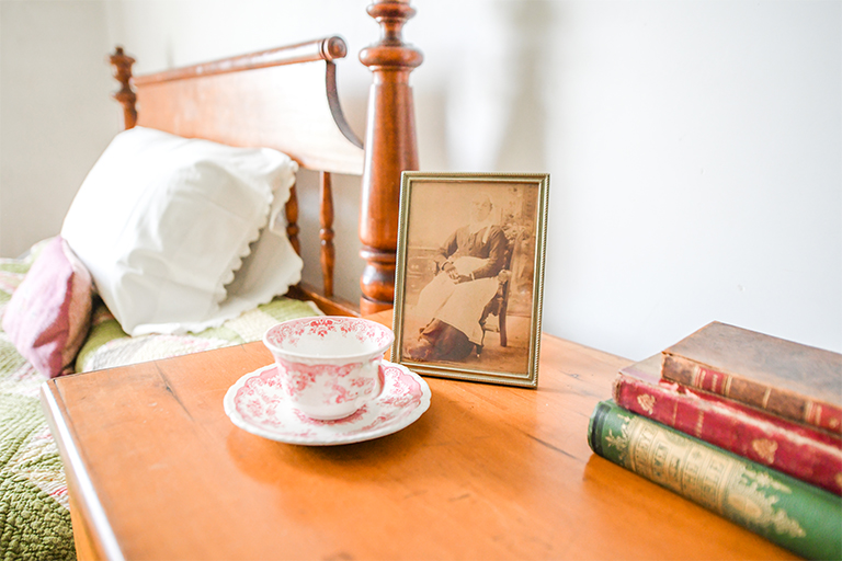A bedside table holds a teacup, antique photo and stack of books