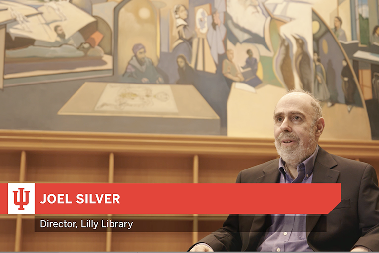 A screenshot still image from a video shows Joel Silver, Lilly Library Director, sitting in front of the Reading Room Murals