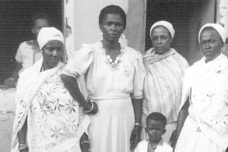 Four women and a little boy stand in front of a dwelling and look ing at the camera.