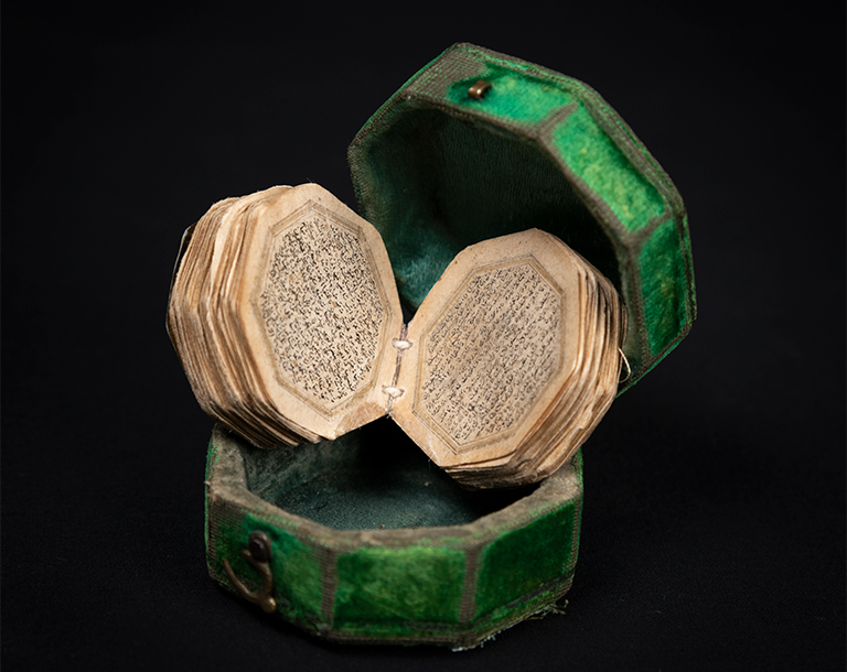 A miniature Qur'an is delicately placed in it's green velvet case and spotlighted from above.