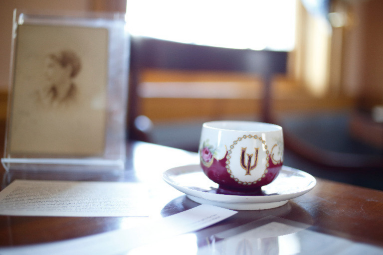 An ornate porcelain IU cup and saucer rest on a table.