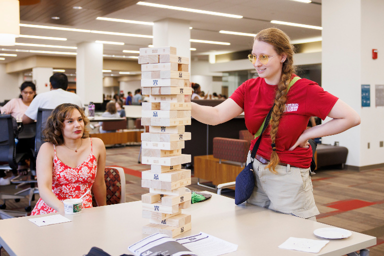 One student reaches to remove a block from a Jenga tower while another looks on.
