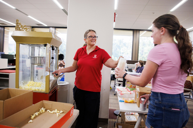 An IU Libraries staff member hands a bag of freshly-popped popcorn to a student.