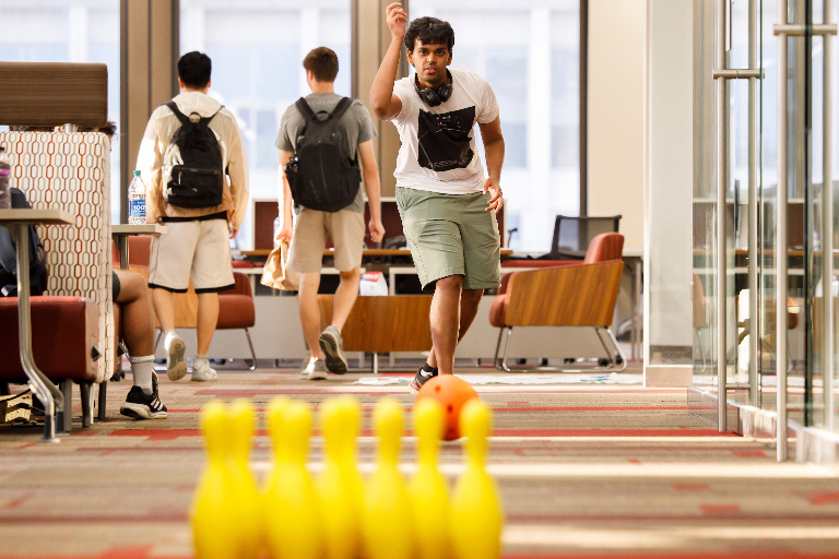 A student has just released a ball towards a set of bright yellow bowling pins. 