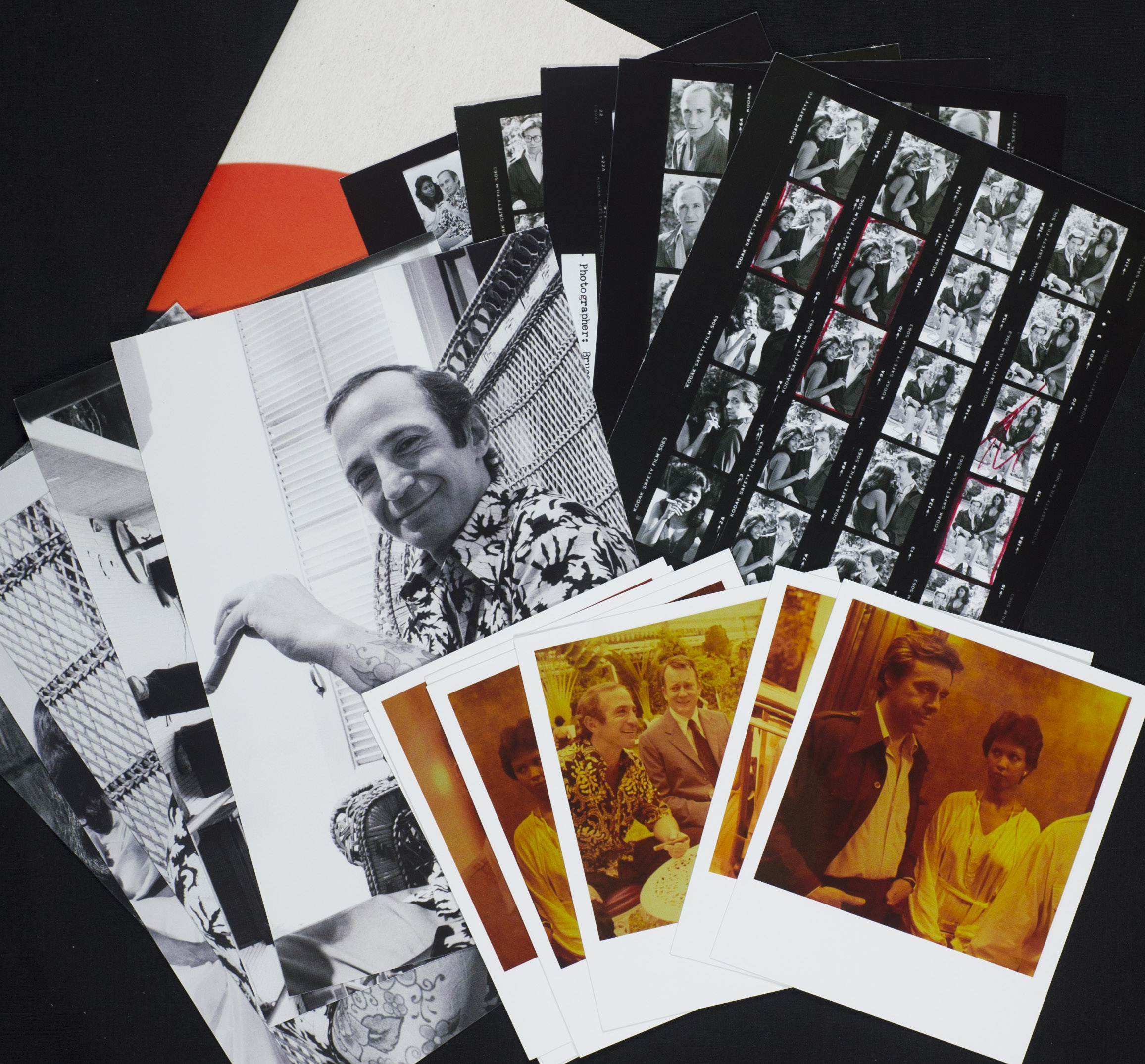 Photos, contact sheets and Polaroid pictures are arranged on a table top.
