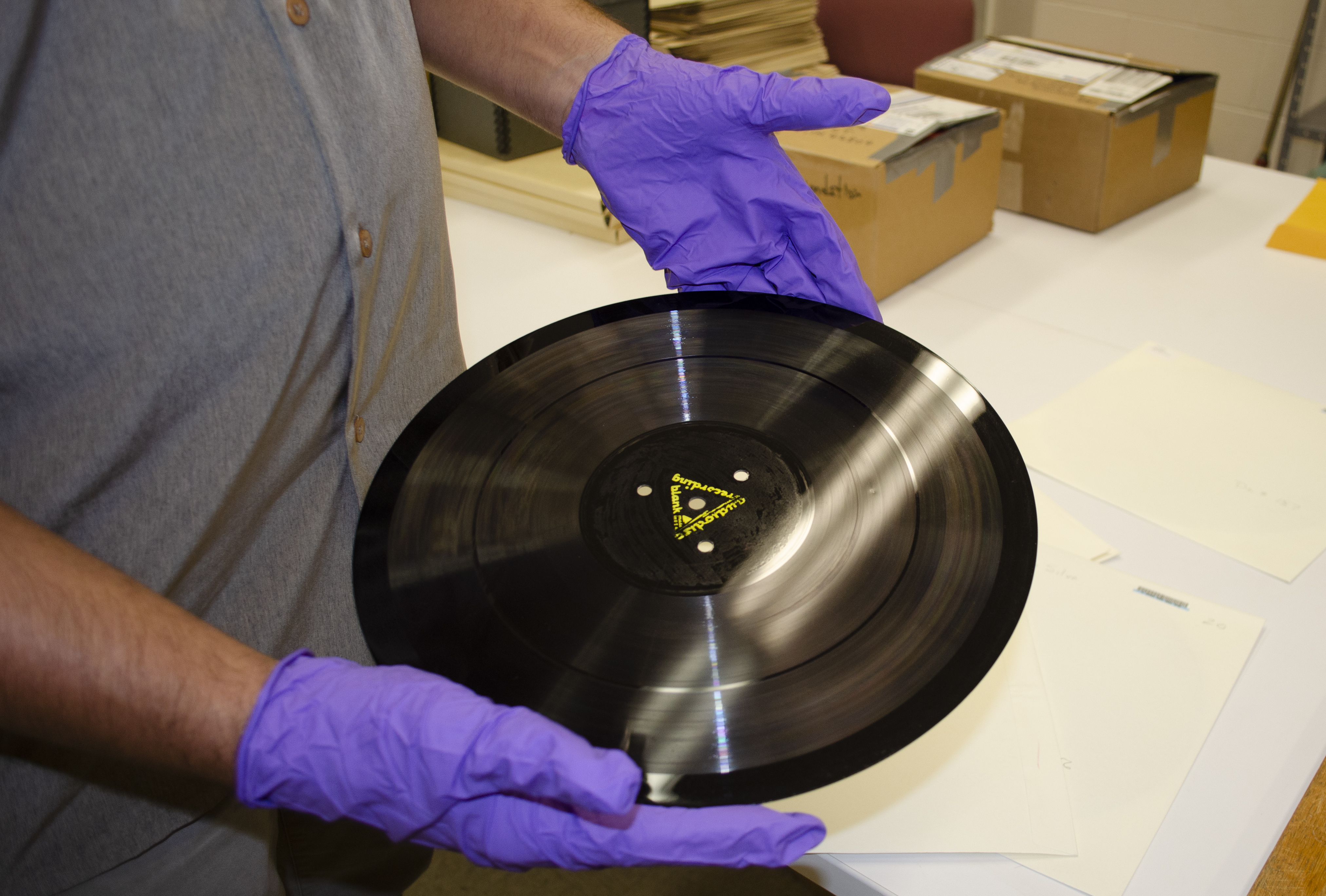 Hands with purple gloves hold a disc recording from the Archives of Traditional Music