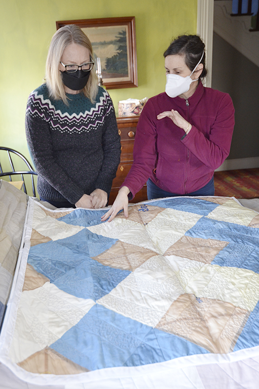 Two pepel are touching a quilt and discussing it together. It is on an antique bed in a historic house museum.