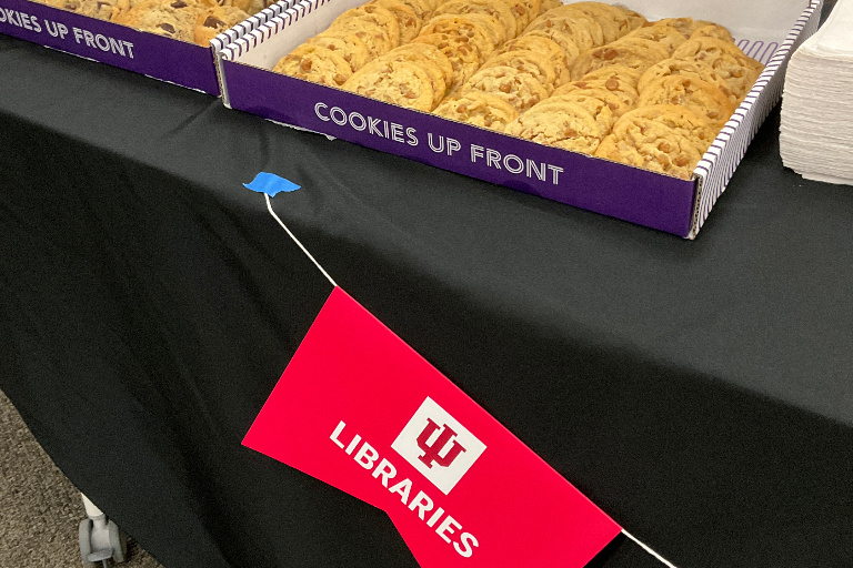 A box of cookies; in front of it hanging from the table is a paper IU Libraries flag.