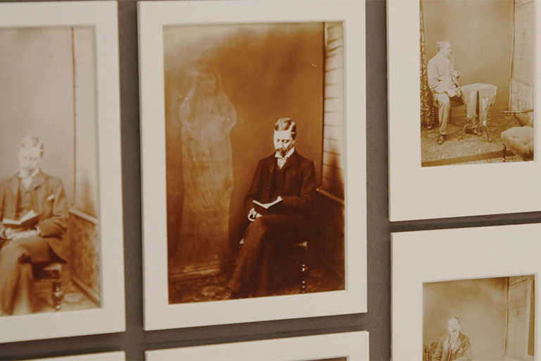 A wall is mounted with several sepia-tone images on matted frames. Some of the images have ghostly figures in the background.