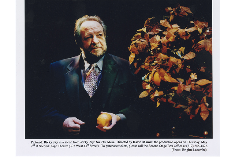 Magician Ricky Jay is shown in a posed photo holding a piece of fruit. The image was promotional for his one-man show, On the Stem.