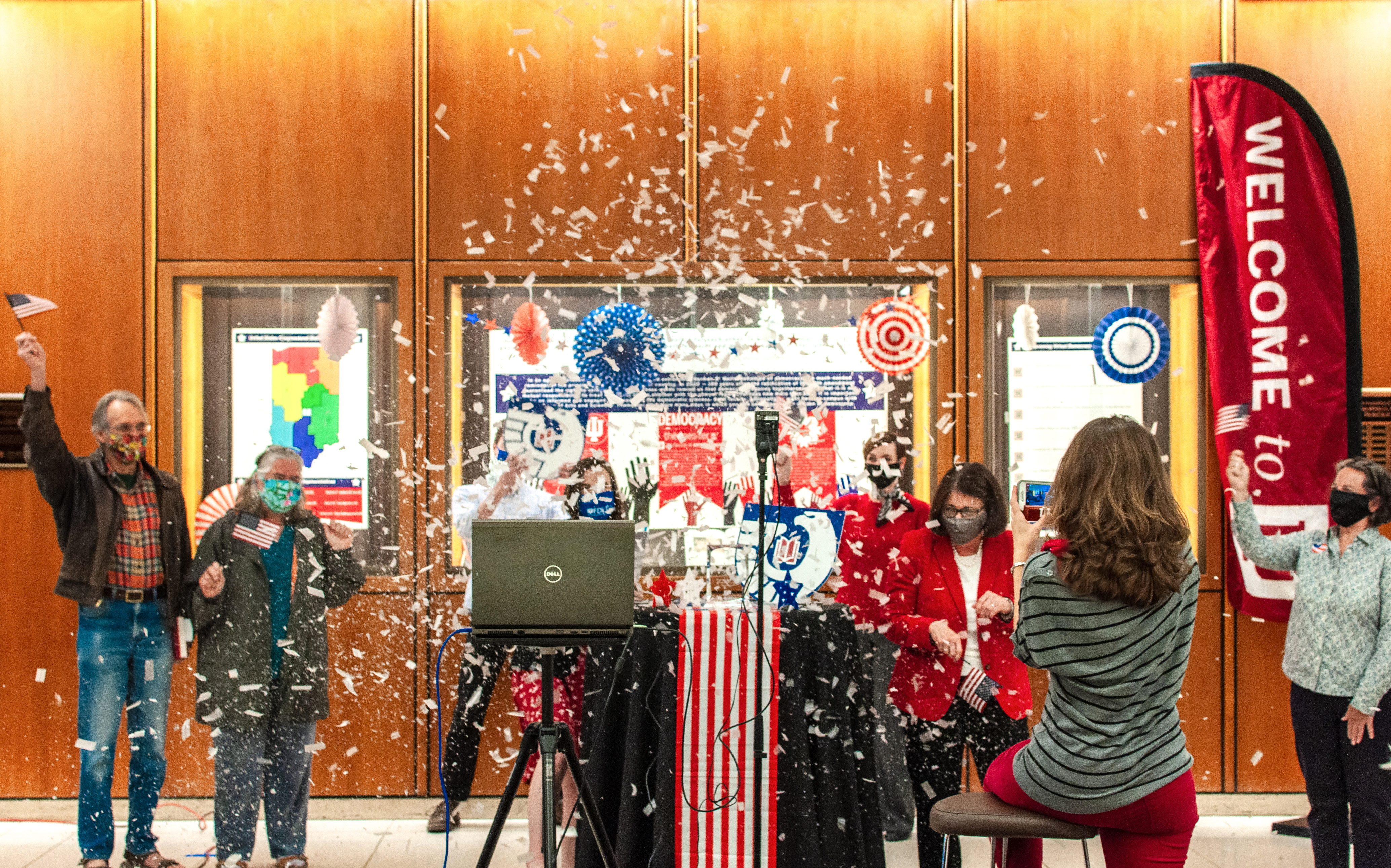A group of people are covered in a shower of confetti as part of a library celebration happening in the Wells Library Lobby