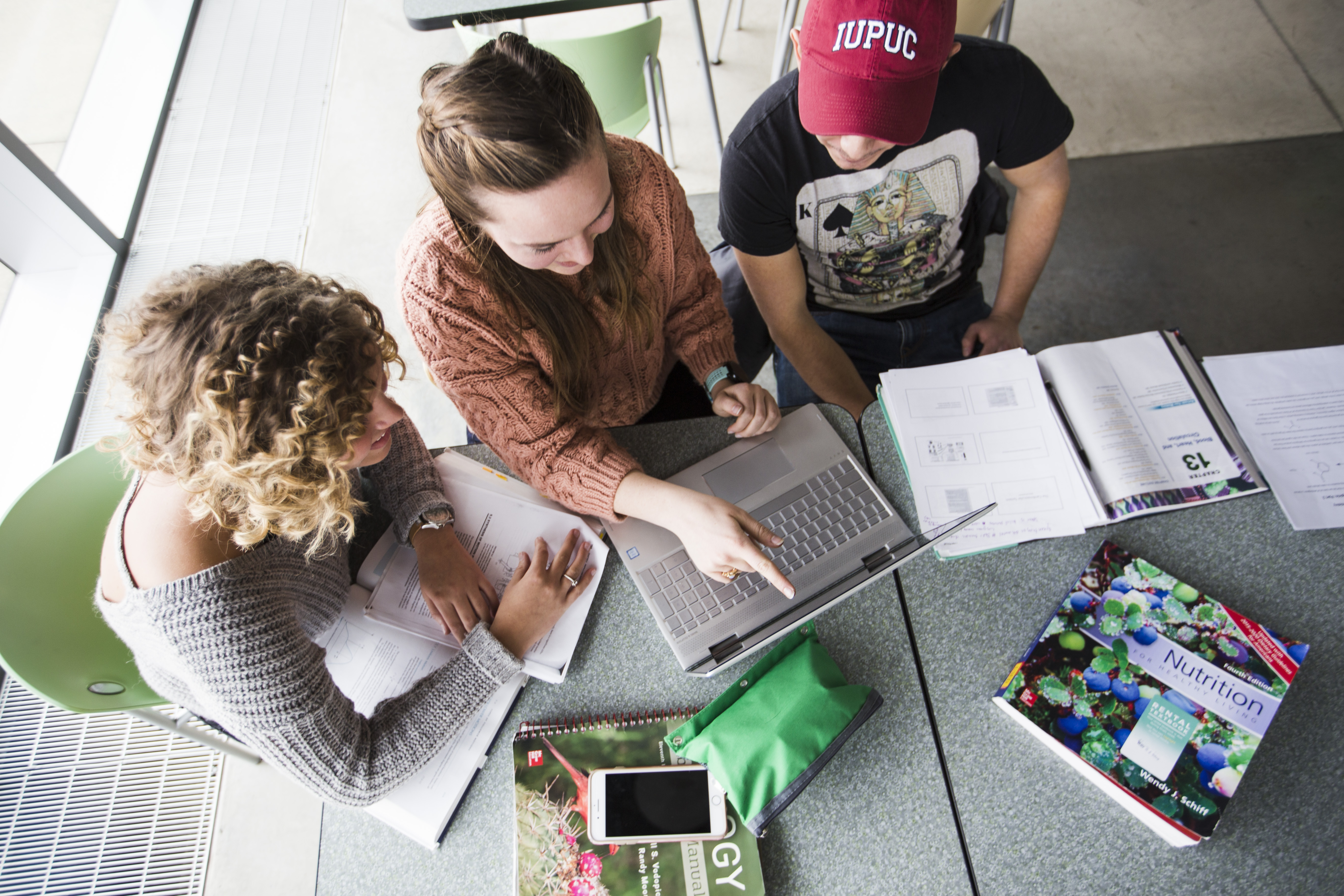 A photo taken from above shows three young adults gathered around a laptop