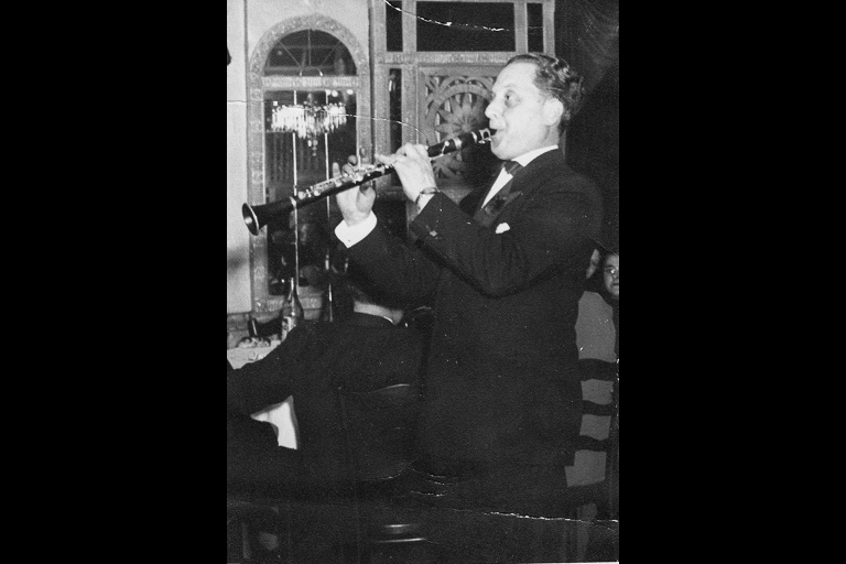 A man in a dress suit plays the clarinet in a fancy ballroom.