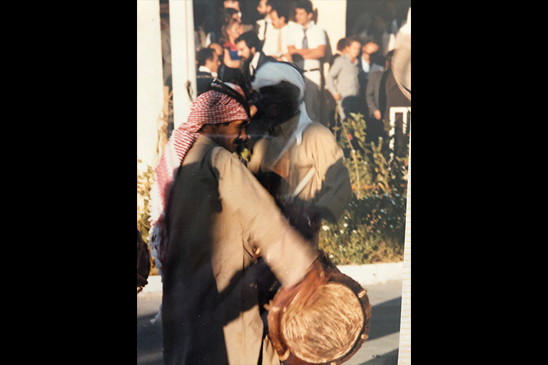 A man uses his hand to beat a drum that hangs horizontally in front of him.