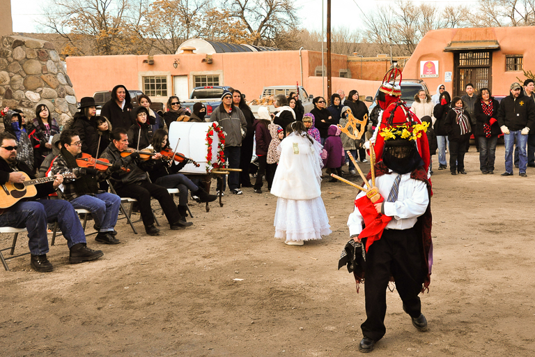 Costumed people dance outside as musicians play and others stand and watch.