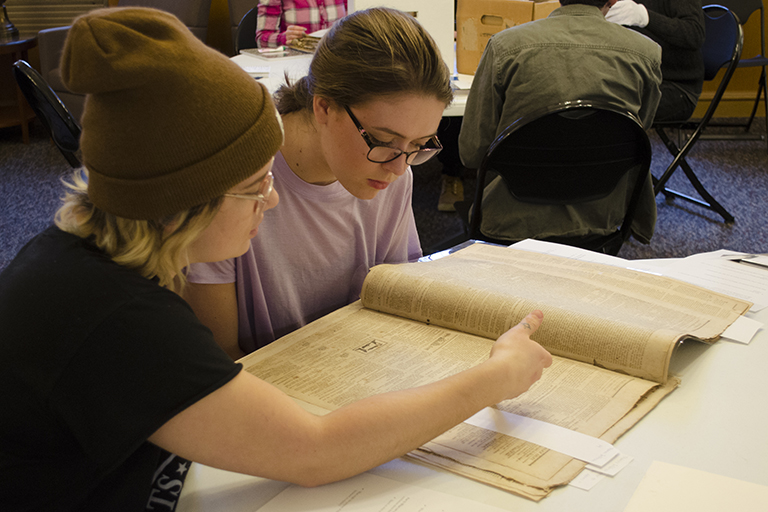 two young women are studying a rare newsprint magazine in a library