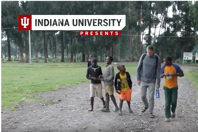 This is a still image taken as a screen shot of a youTube video.  It shows Mike Courtney with students in Rwanda.
