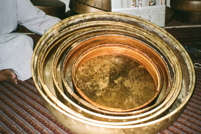 A nested set of golden brown hand drums sit on a striped rug.
