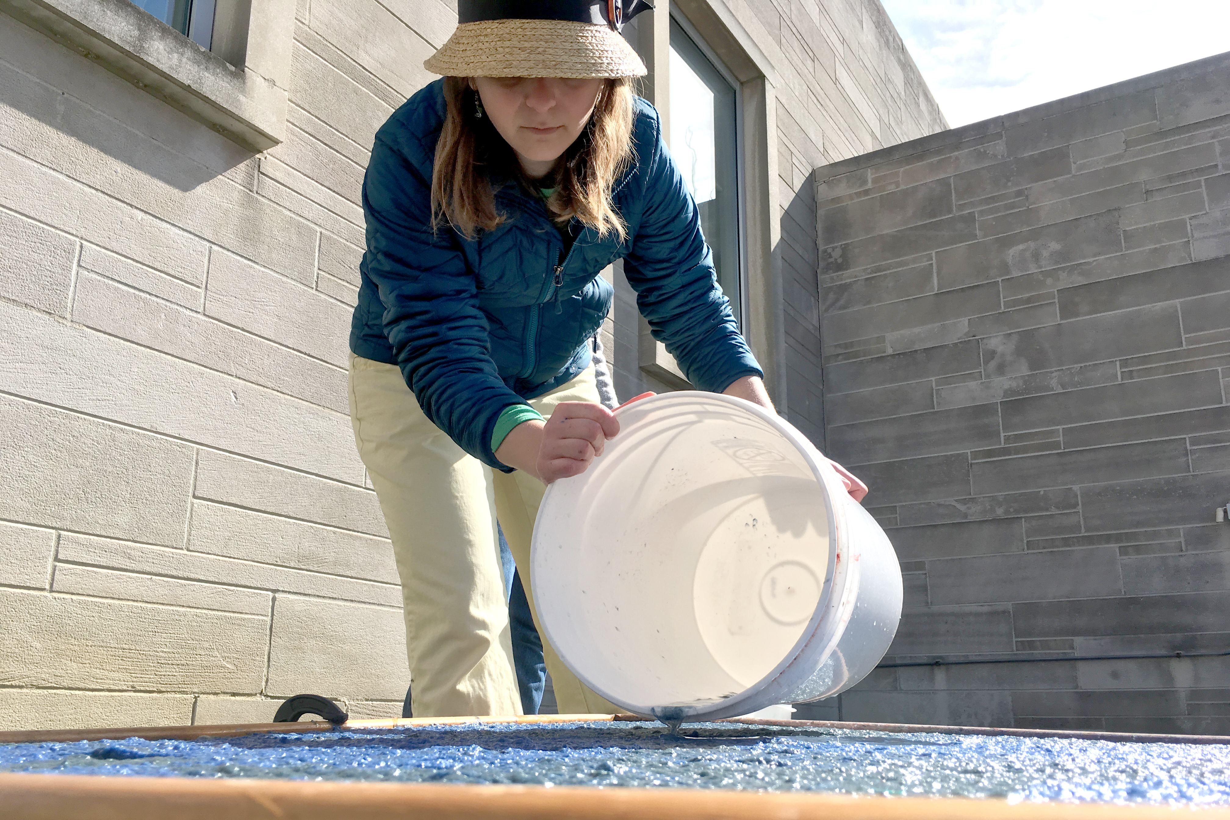 Artist Laura Post is shown outdoors pouring liquid from a bucket