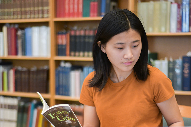 A female student is shown in the Lilly Library Reading Room holding a book.