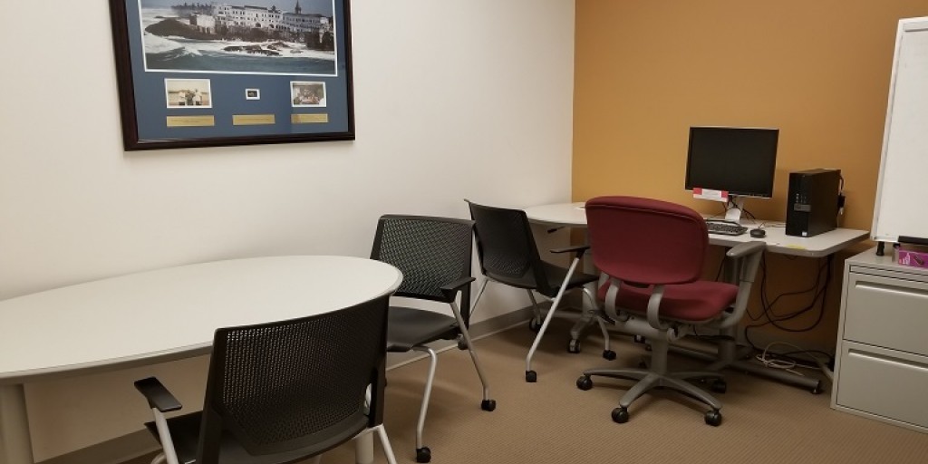 Small oval table with two chairs and a computer workstation on a separate table with two chairs
