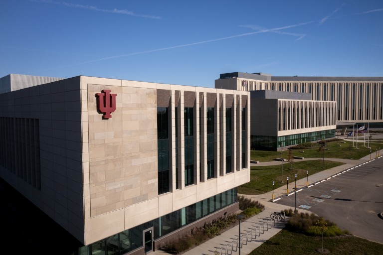 A towering limestone building with the IU trident stands against a blue sky.
