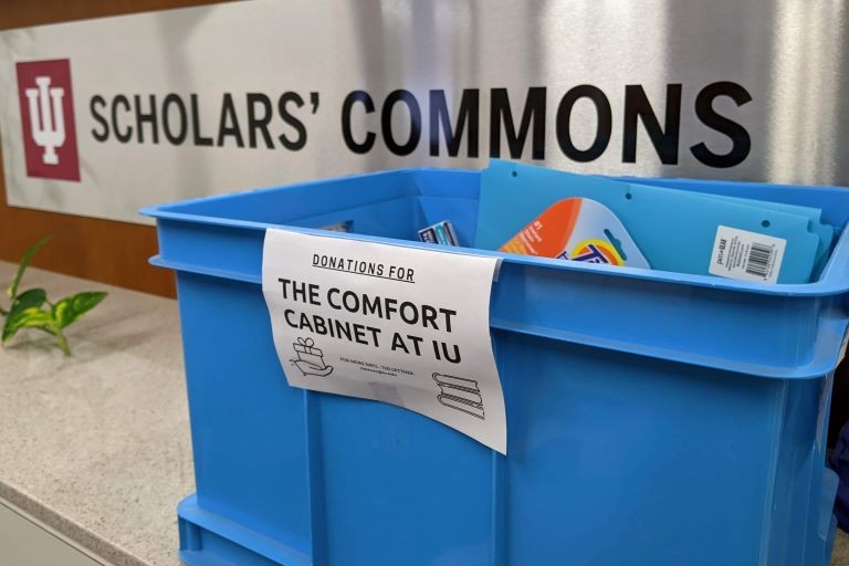 A blue plastic crate with a sign that reads, "Donations for the Comfort Cabinet."