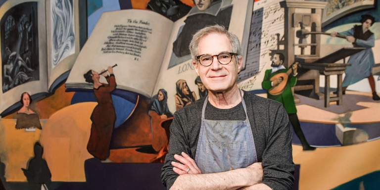 Artist Ralph Gilbert stands with his arms crossed in front of one of the Lilly Library mural panels