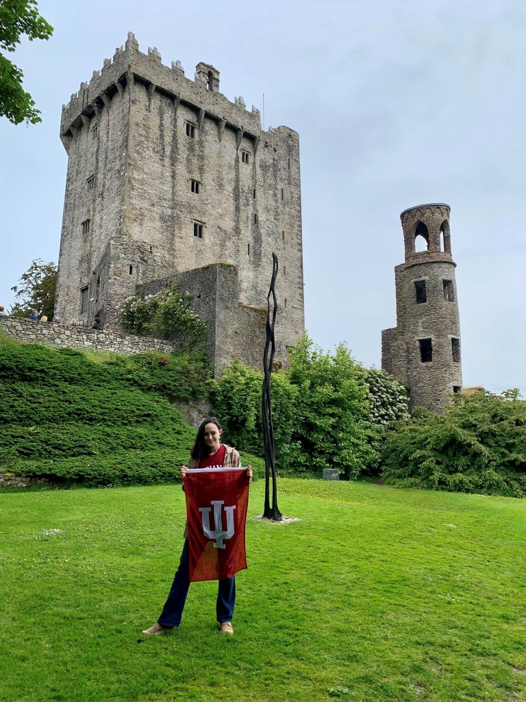 Joelle stands in front of the ruins of an old castle with an IU flag.