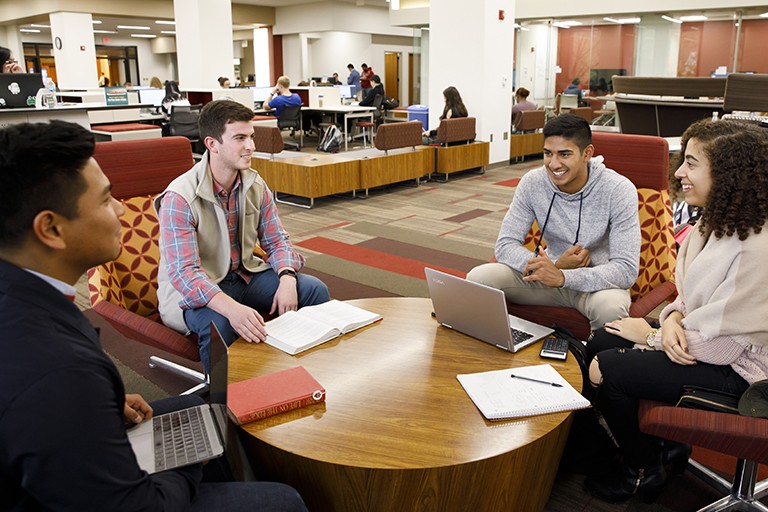 Four students are gathered around a small table in a library.