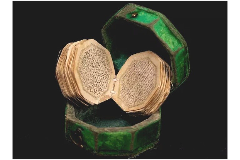 A tiny manuscript Quran with round pages in a octagonal green case.