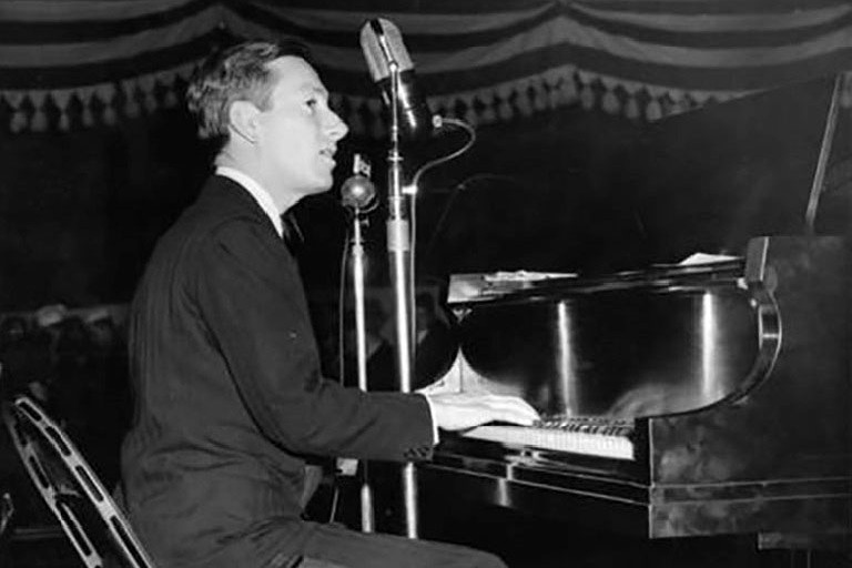 Hoagy Carmichael on a stage, playing a piano and singing, in the 1930s.