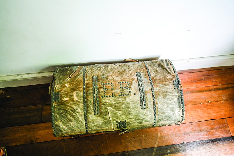 An antique trunk is pictured from above. The initials E.B. are set into the top with metal rivets