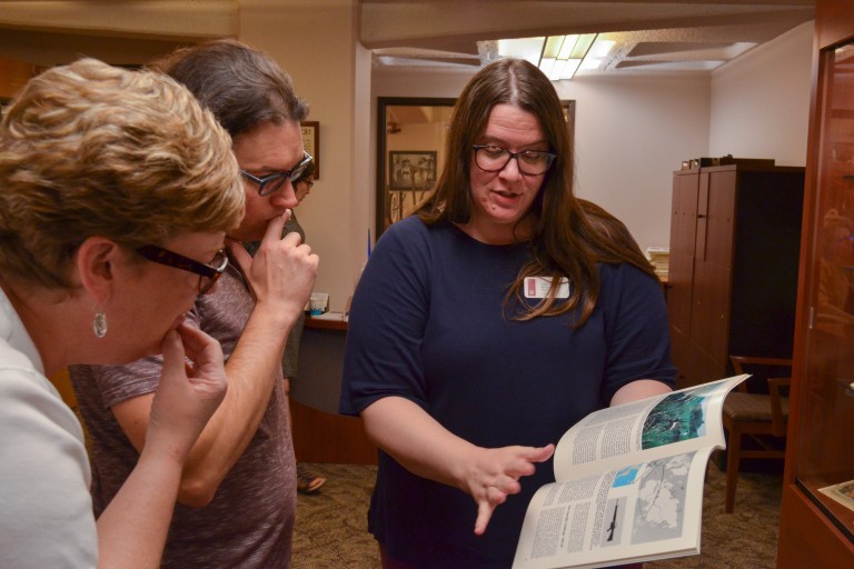 A woman showing a book to two individuals.