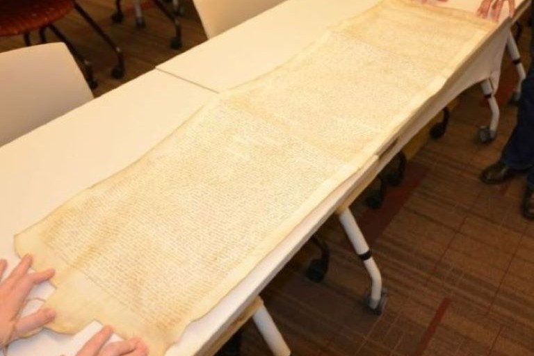 A long scroll unrolled on a table. It's covered in cursive handwriting.