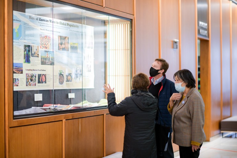 Three individuals inspecting a poster behind glass.