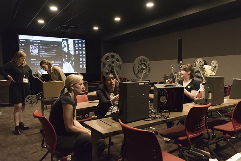 several students are in a darkened film screening room working with projectors.
