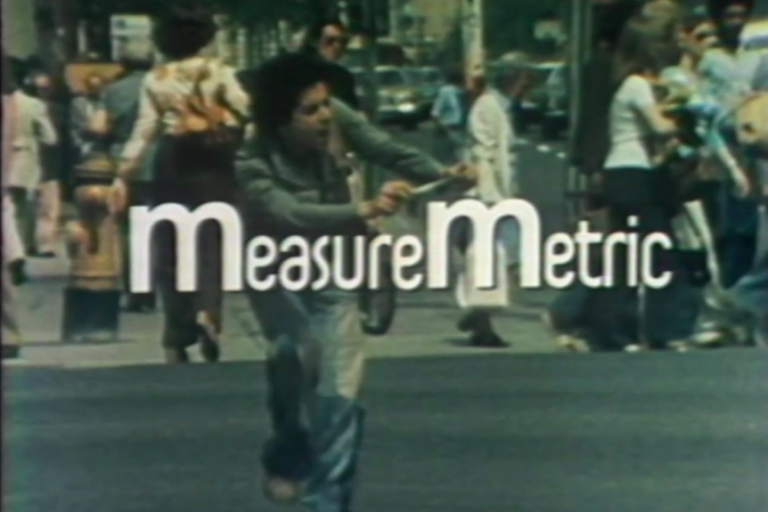 Title screen for Measure metric, shows the title in white font with an image of a man on a city street walking around with a measuring tape